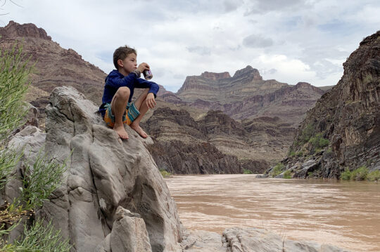 A child sitting on a rock next to the Colorado River