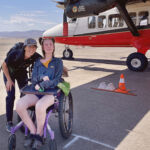Woman in a wheelchair smiling under the wing of an airplane