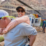 Man carrying a paraplegic woman on his back with a helicopter in the background.