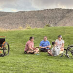 People sitting in grass with wheelchairs nearby