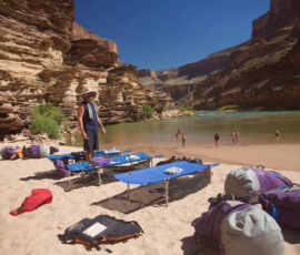 A man standing near his cot with the Colorado River behind.