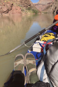 A person wearing wool socks and river sandals while in an oar boat.