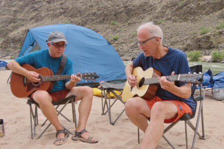 Two men playing guitar in camp.