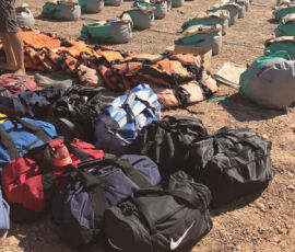 Duffel bags on a beach with dry bags behind.